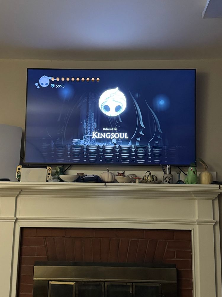 A picture of a TV showing a still shot of Hollow Knight. There is a large icon on the screen with the caption “collected the Kingsoul”