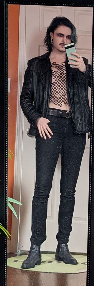 Me taking a mirror selfie. I'm wearing a leather jacket, mesh torn shirt, black jeans, and Chelsea boots. My mirror desperately needs to be cleaned 