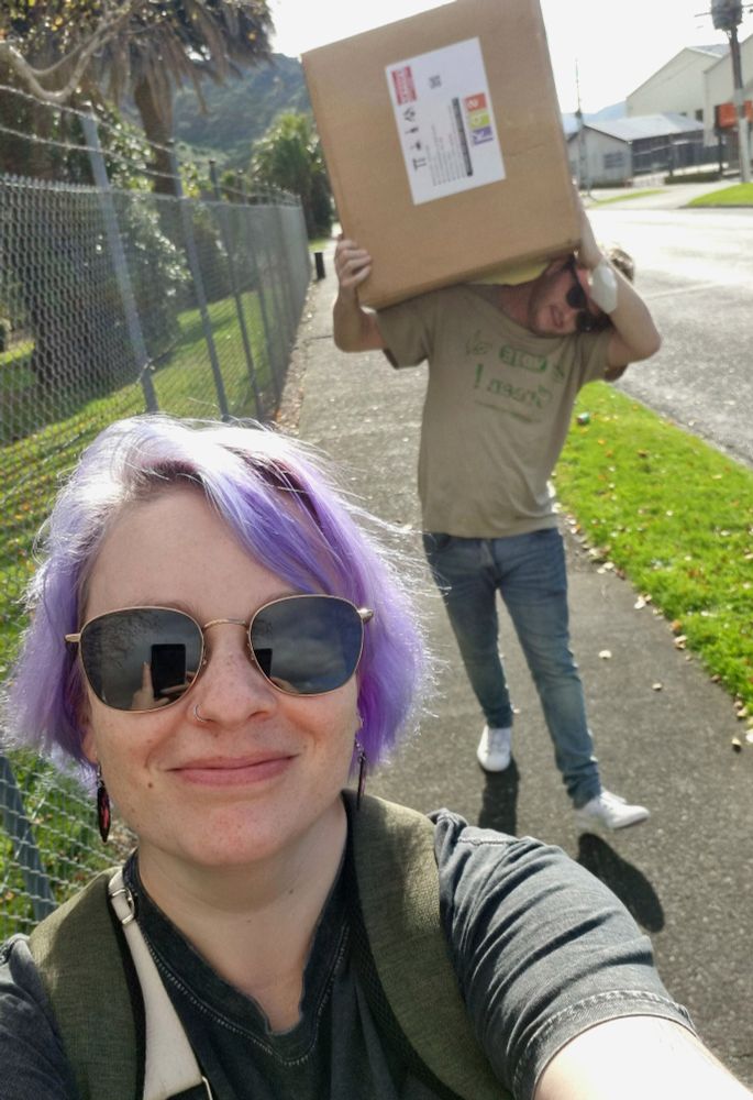 A selfie of Louise walking down the street with her partner behind her carrying a giant box on his shoulders
