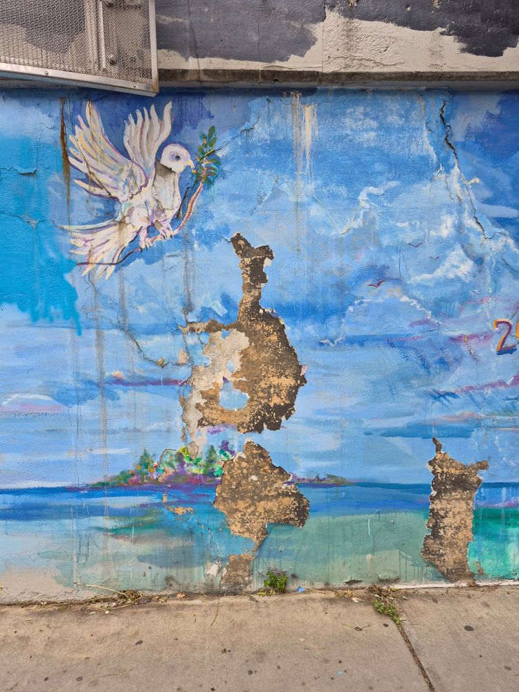 Mural of a dove and blue sky with several chunks of wall missing