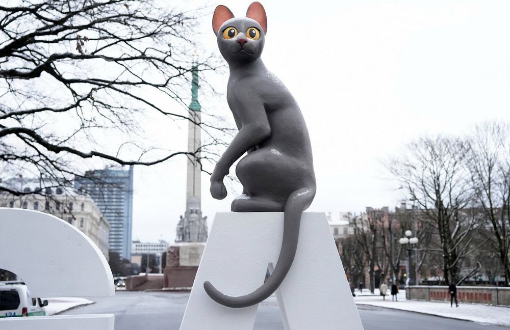 estátua do gatinho preto do filme flow numa praça em riga, na letônia. o gatinho tá sentado em cima da letra A de riga. ao fundo, tá nevando 