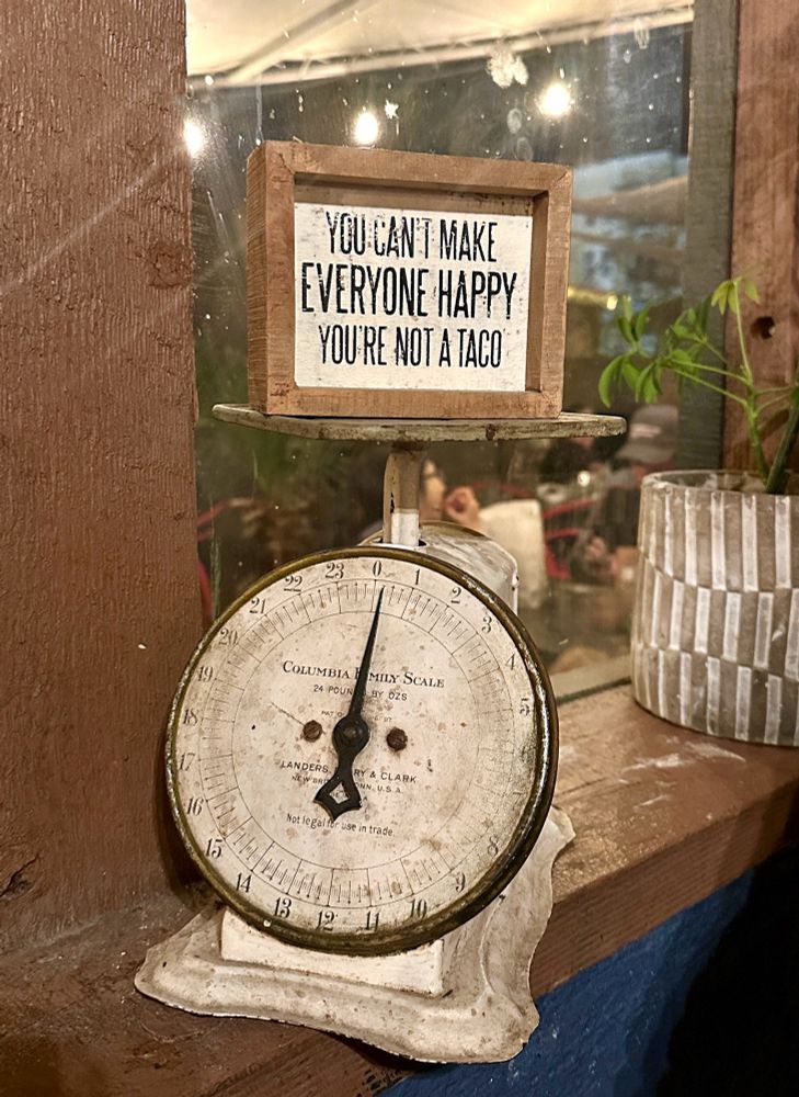 A sign on an old scale reads: You can’t make everyone happy, you’re not a taco