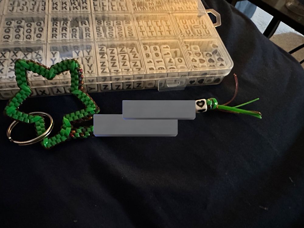 Image of a homemade zipper pull with a star shape on the left and a key ring attached, with a name blocked out followed by a heart bead. 