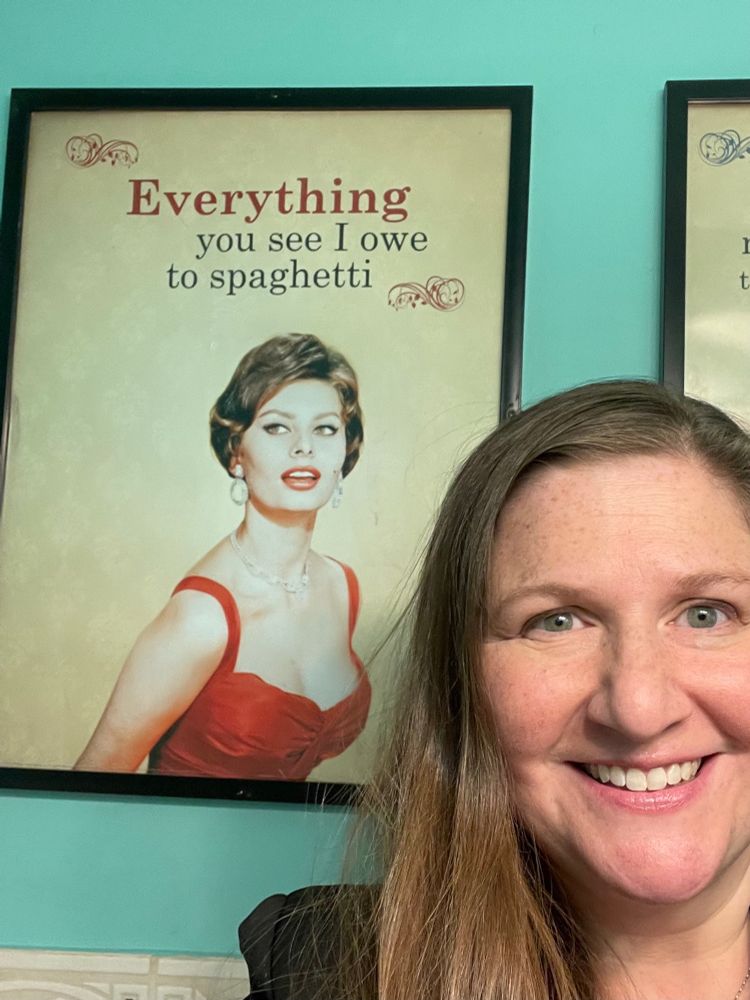 Photo of Julia in front of poster that says “everything you see I owe to spaghetti”
