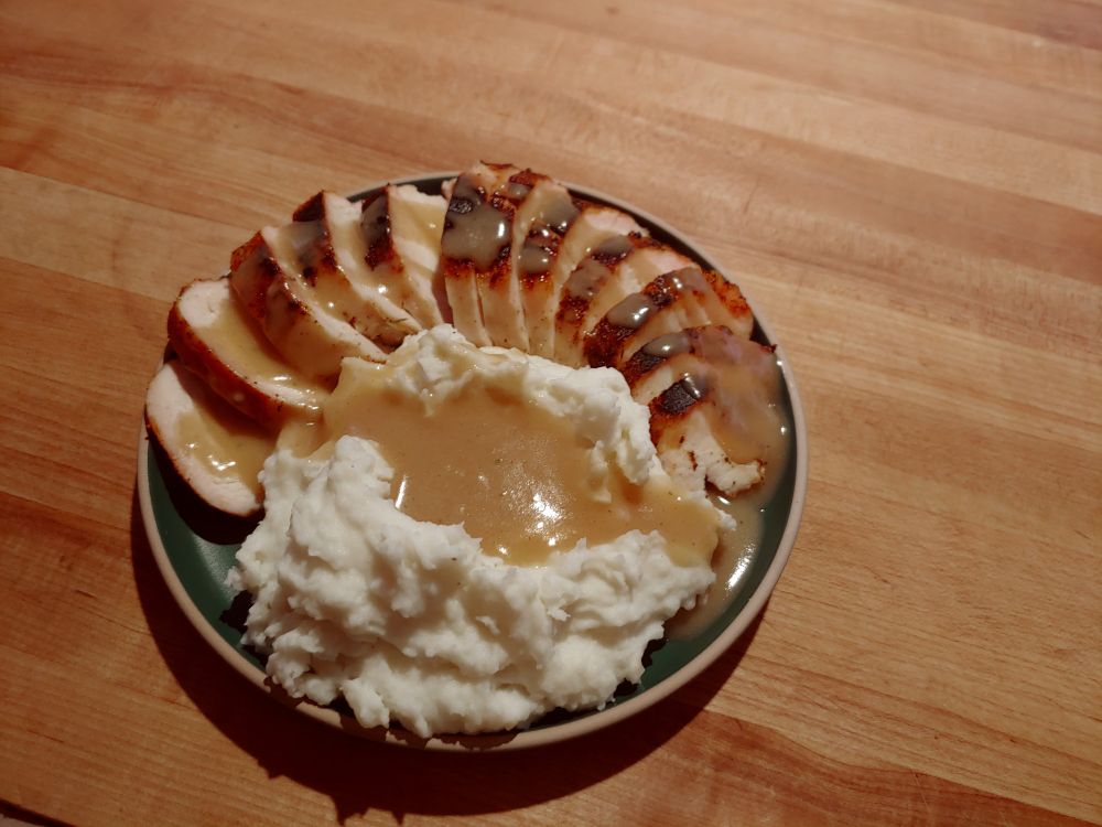 Oven roasted chicken and mashed potatoes, arranged on a green plate on a butcher block counter top.