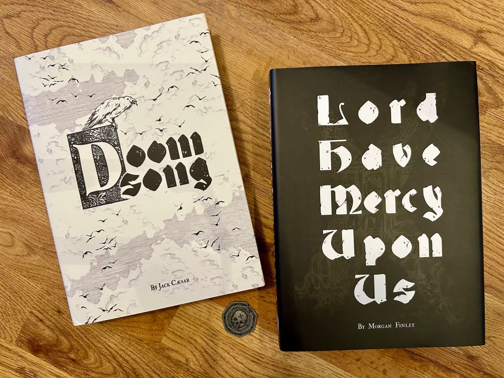 Copies of the Doomsong core rulebook and the campaign book Lord Have Mercy Upon Us with the Doom Coin next to them.