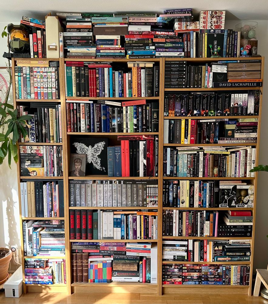 2 1/2 IKEA Billy shelves back to the brim with books, with additional stacks on top reaching the ceiling.