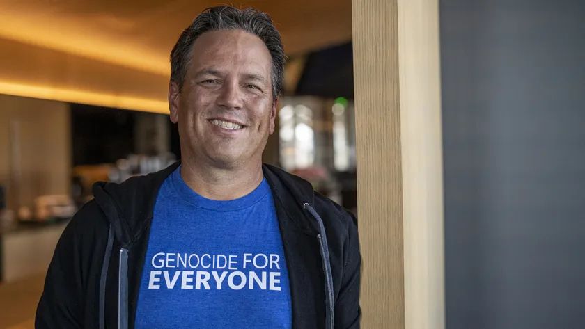 photo of Microsoft's Phil Spencer standing in a doorway while smiling and wearing a blue shirt with what looks to be a black jacket or hoodie. The text on the shirt originally said "GAMES FOR EVERYONE" but has been edited to say "GENOCIDE FOR EVERYONE" because of Microsoft's involvement with Israel/the IDF in the ongoing atrocities in Palestine. Fuck Phil Spencer and fuck Microsoft.