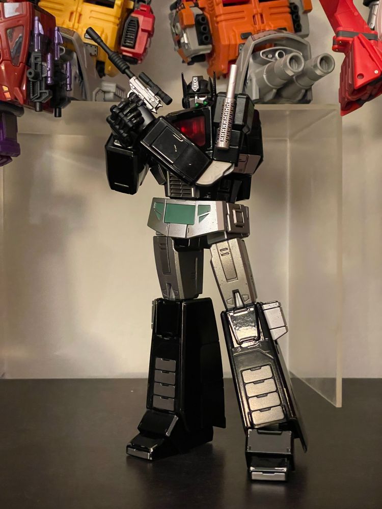 Yolopark AMK Pro Nemesis Prime standing with a slight lean while holding a very Megatron-like firearm in his left hand and supporting his grip with his right hand.
