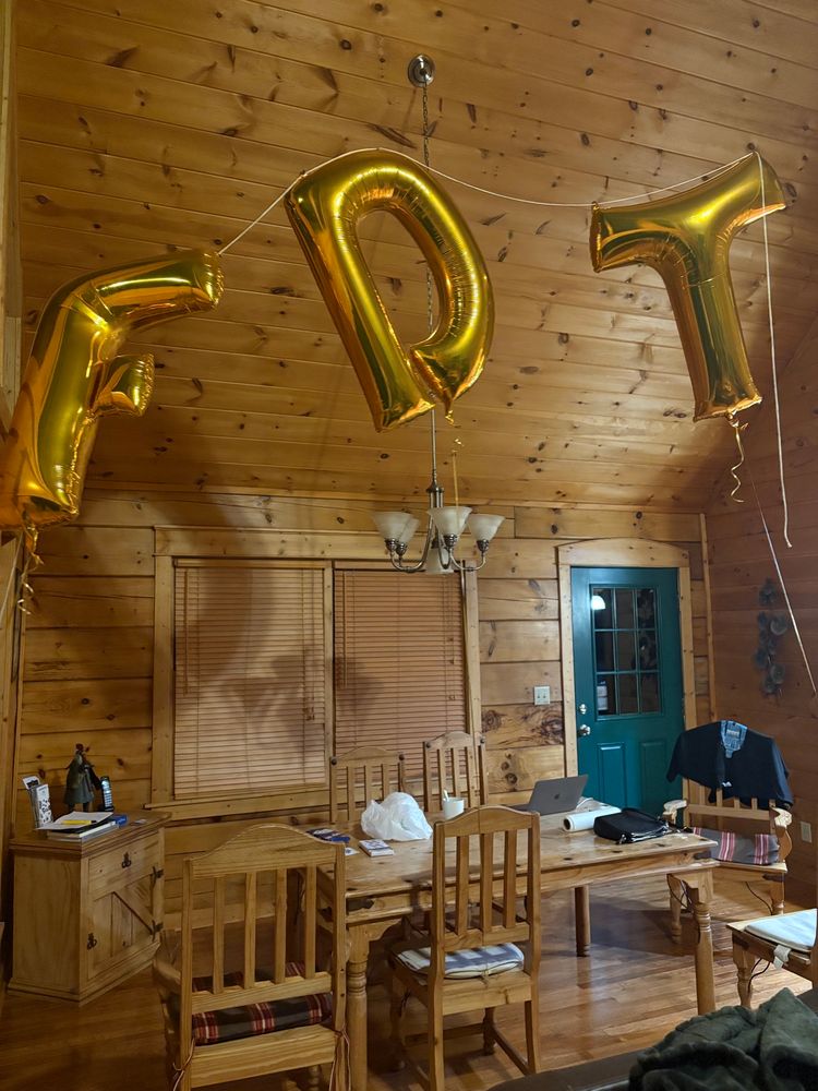 Three helium-filled giant gold Mylar balloons spelling out FDT float in a high-ceilinged cabin 