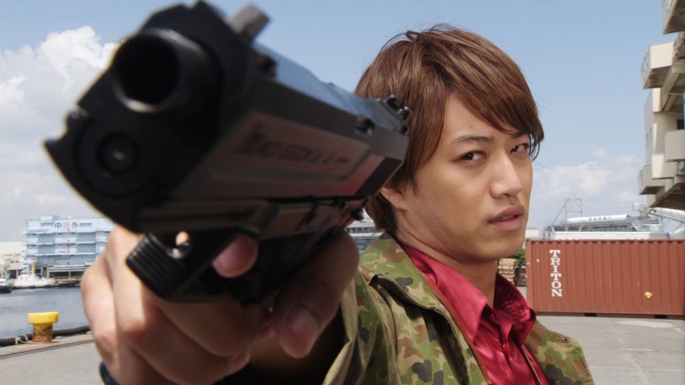 Tsukasa Kadoya, o Kamen Rider Decade, em sua aparição comemorativa na série de Zi-O 10 anos depois. Ele está segurando uma arma de verdade e apontando ela para a tela num angulo ameaçador