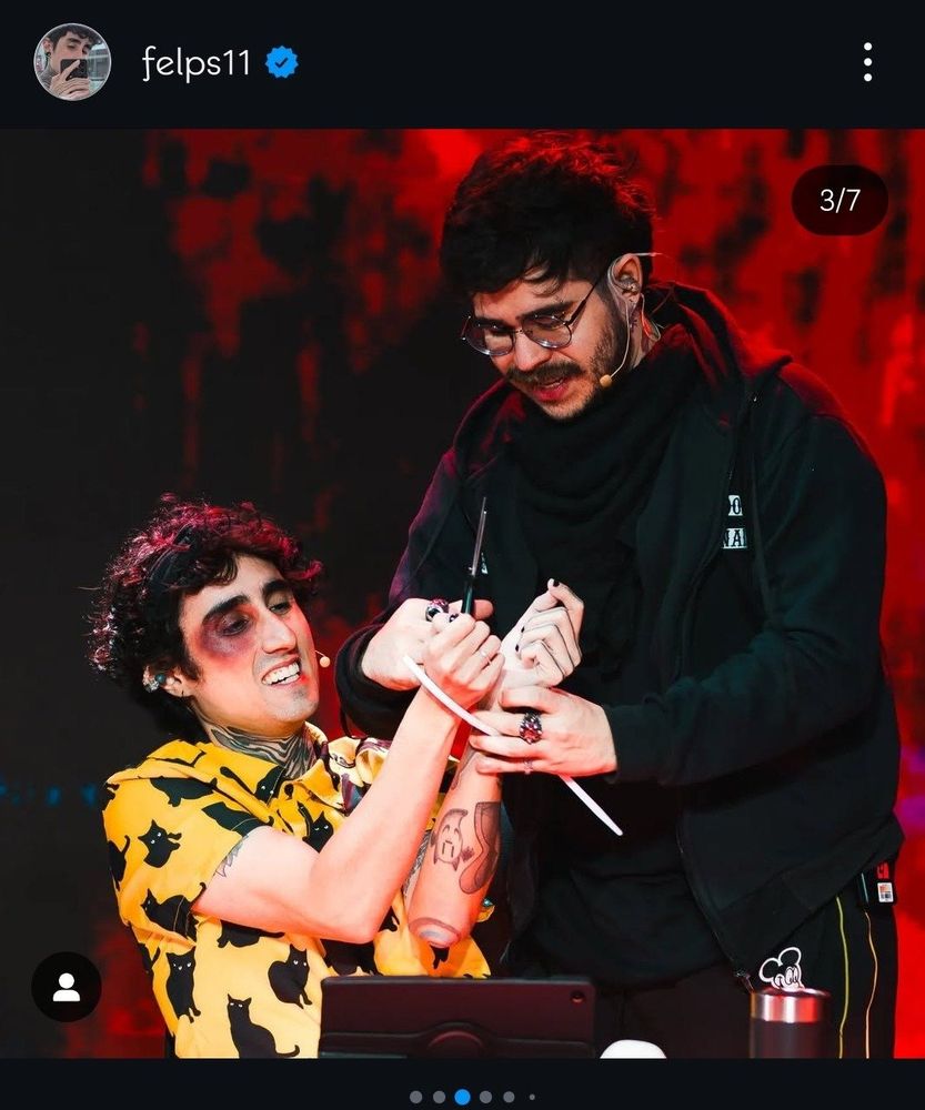 foto do felps e do guaxinim. o felps está sentado com os pulsos amarrados e uma maquiagem de olho roxo e o guaxinim está em pé cortando a fita que está prendendo o felps