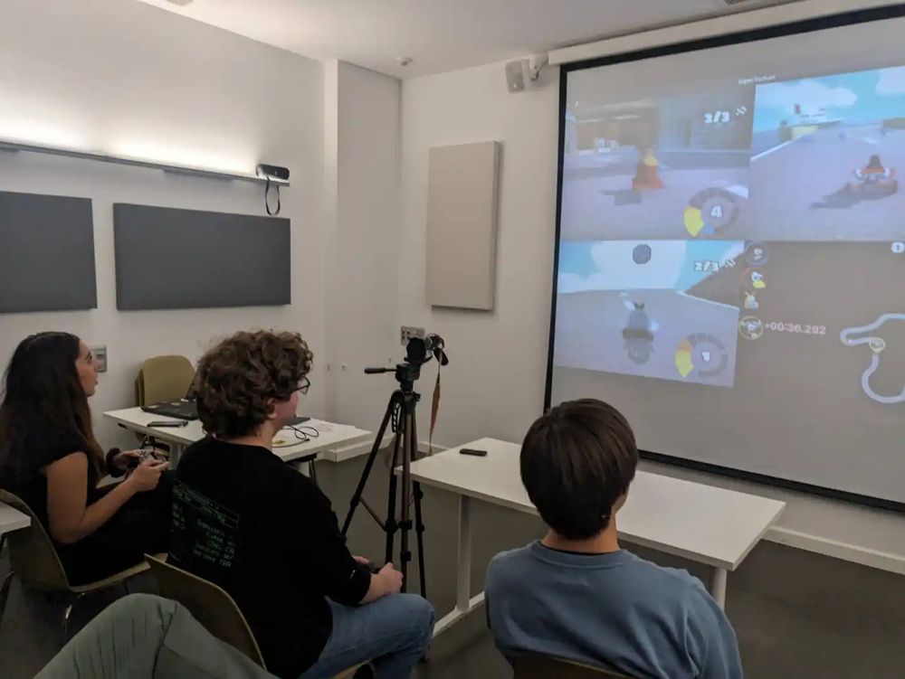 3 personas juegan a Super Tux Kart en pantalla dividida en un projector de aula.
