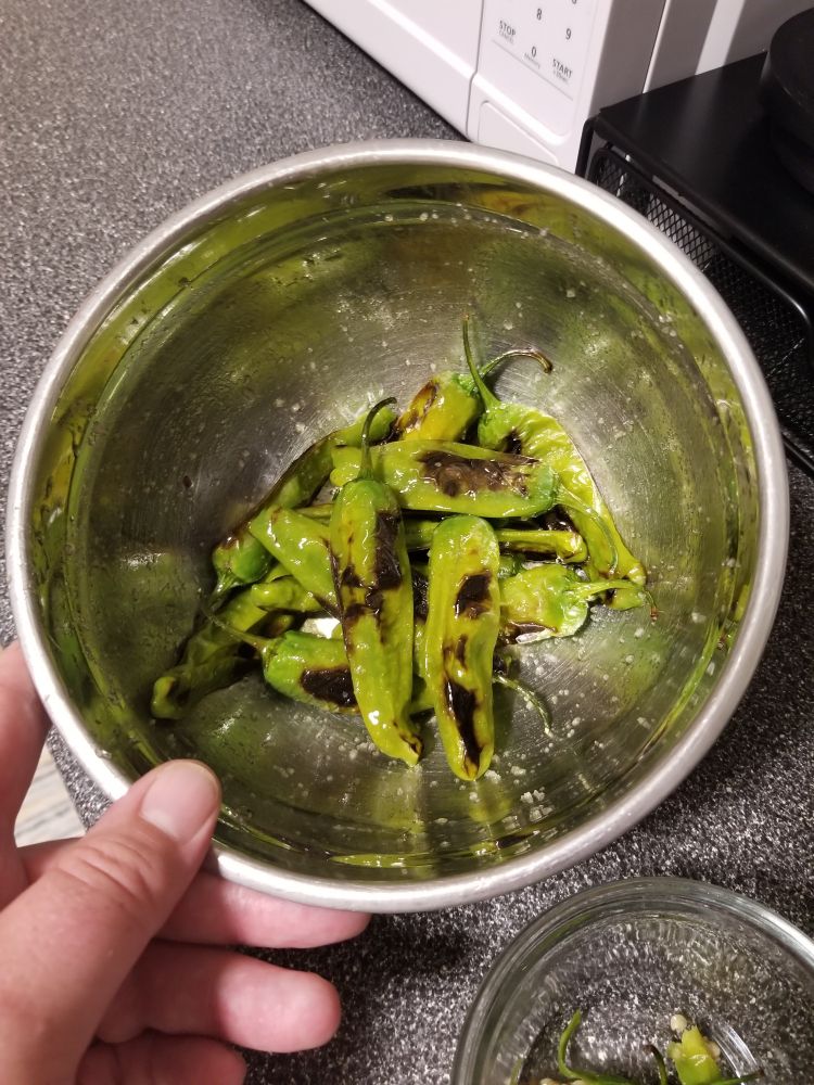 Blistered shishito peppers with some olive oil and flaky salt in a metal bowl
