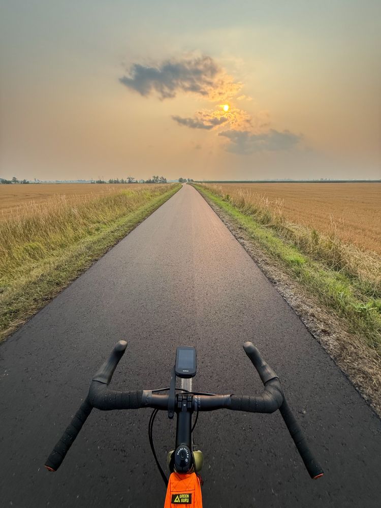 A smokey sunset over the countryside. A gravel bike is riding on the fresh resurfaced rail trail. 