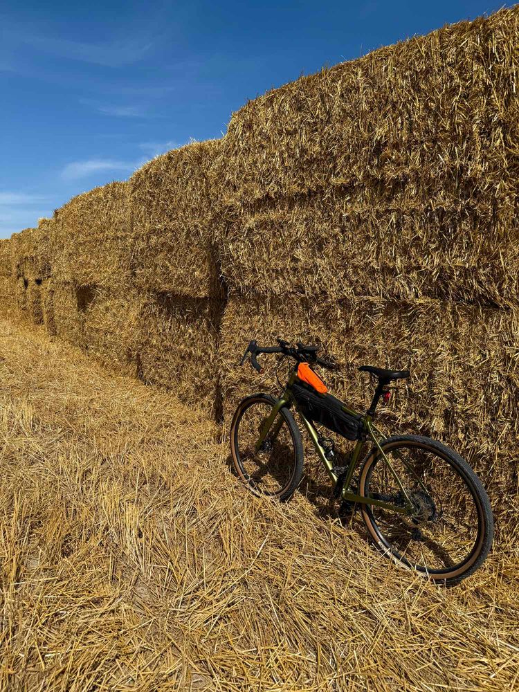 A gravel bike leaning against stacked bales of hay on a sunny day. 