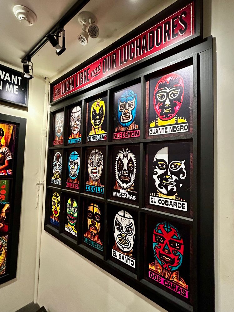 Giant colourful wall plaque adorned with depictions of the masked faces of various luchadores, including El Santo Dos Caras, Blue Demon, El Ídolo, etc