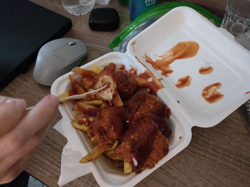 A box of 5 chicken nuggets, one half-eaten, and several fries, with BBQ sauce