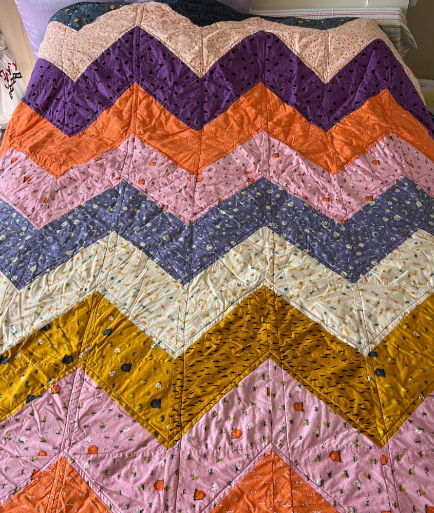 A very wrinkly Halloween quilt with many different printed fabrics in purple, orange, cream, and gold 