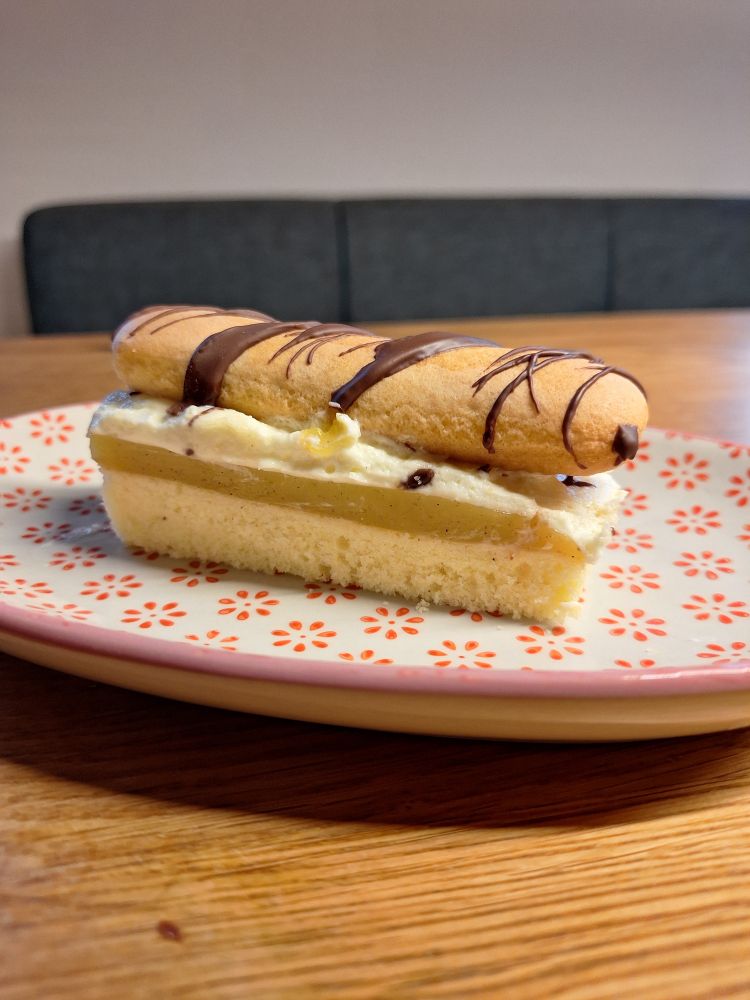 Lambadaschnitte: Sandmasseboden, Orangenpudding, Schlagobers und eine Biskotte inkl. Schokoverzierung; auf einem Teller mit kleinen roten Blümchen