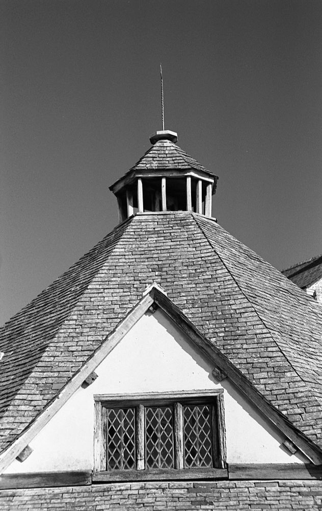 A black and white photo looking at the roof and leaded window of Dunster Yarn Market. 