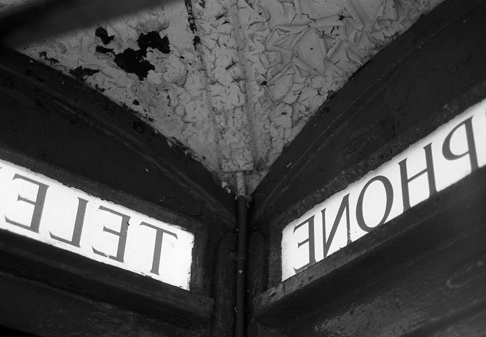 A black and white photo looking up at the corner of a disused telephone box with two halves of the telephone sign reversed.