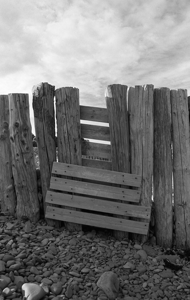 A black and white photo looking at a repair made to one of the groynes. A post is missing and wooden planks have been nailed across the gap.