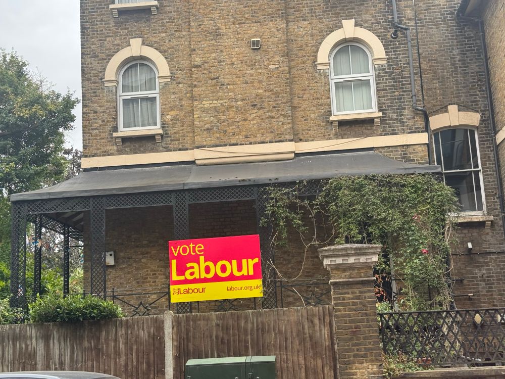 A house with a bright red sign and yellow text reads, “Vote Labour”.