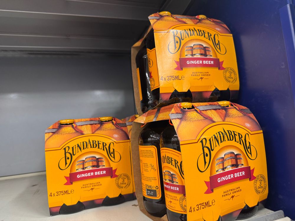 Some four-packs of Bundaberg Ginger Beer sitting on a grey supermarket shelf.