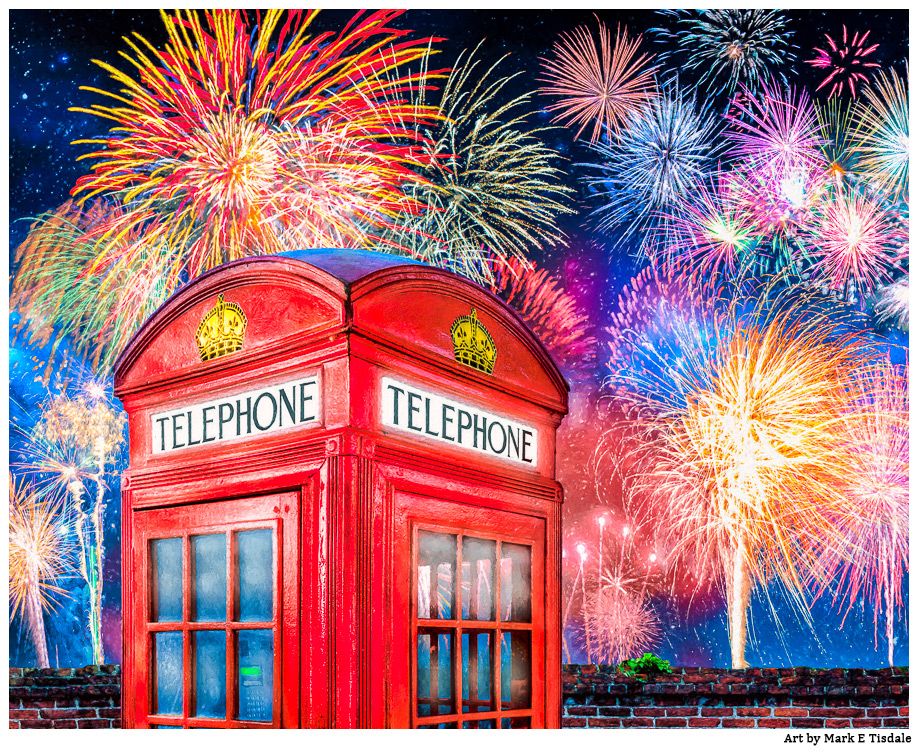 The top 2/3 of a red British telephone booth standing next to a brick wall with fireworks in the night sky beyond it. 