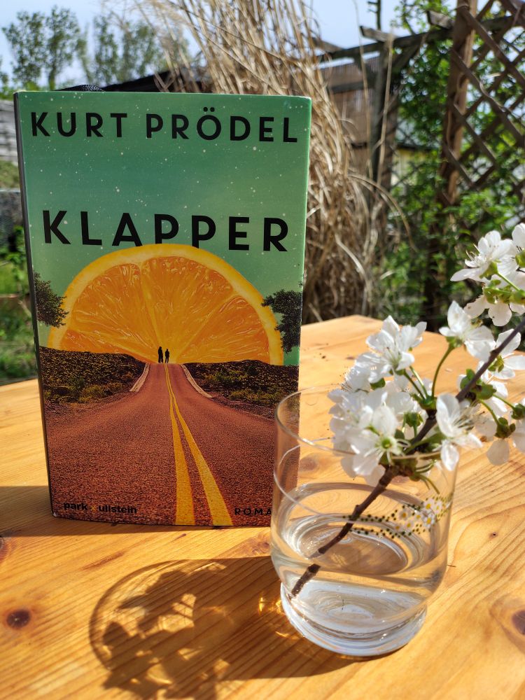 Das sehr gute Buch von Kurt Prödel in der Frühlingssonne auf einem Holztisch neben einem kleine Ast mit blühenden Kirschblüten in einem sehr sehr alten Glas.
