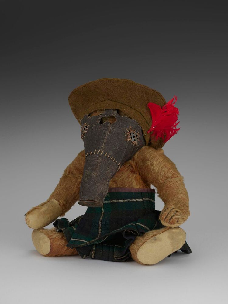 Brown mohair plush fully jointed teddy bear. The eyes are black boot button and the nose, mouth and claws stitched with black wool. There is the Steiff trademark metal button in the left ear. The accessories are two kilts, a beret, a houndstooth suit comprising jacket, trousers and hat, and a homemade metal and cloth gas mask.