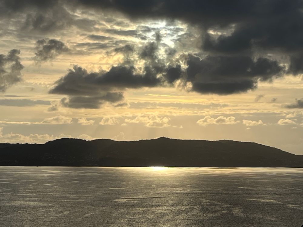 Dramatisch-wolkiger Himmel über einem fast schwarzen Bergrücken, davor das Wasser des Fjords vor Bergen mit einem hellen Sonnenstreif.