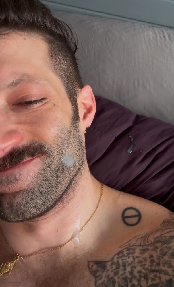 A close up selfie of RJ smirking in bed. He has what appears to be Toaster Strudel icing on his cheek, neck, and pillow 🤭 