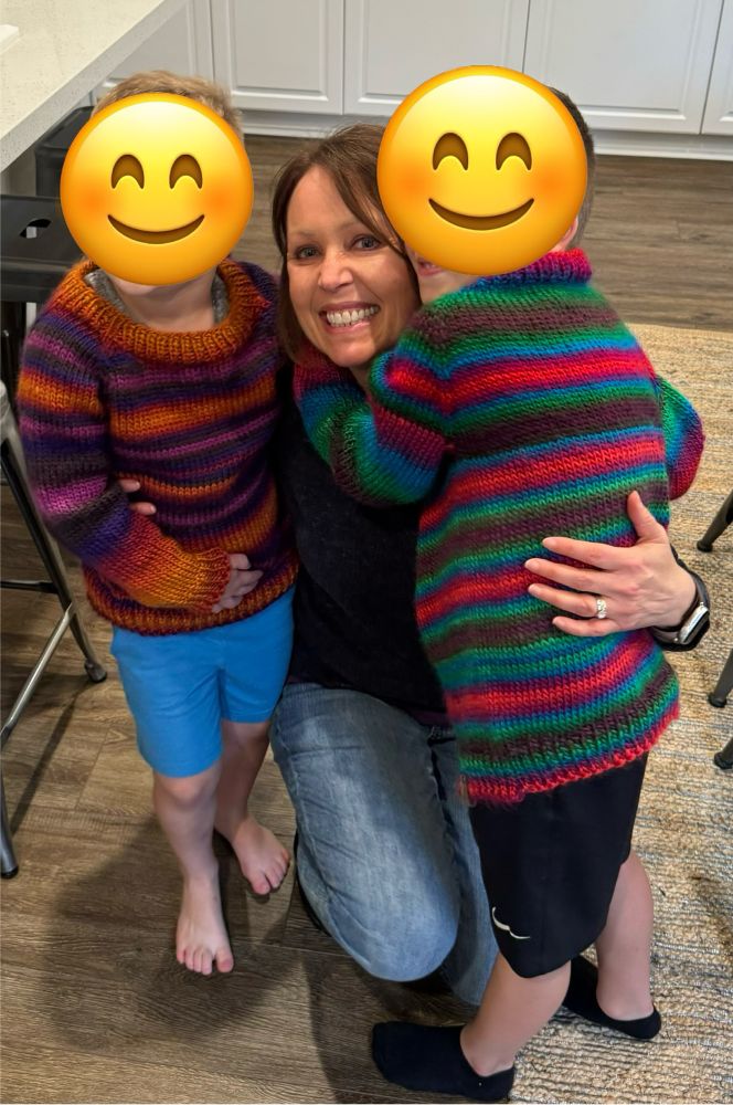 A knitter hugging two boys with their new sweaters. 