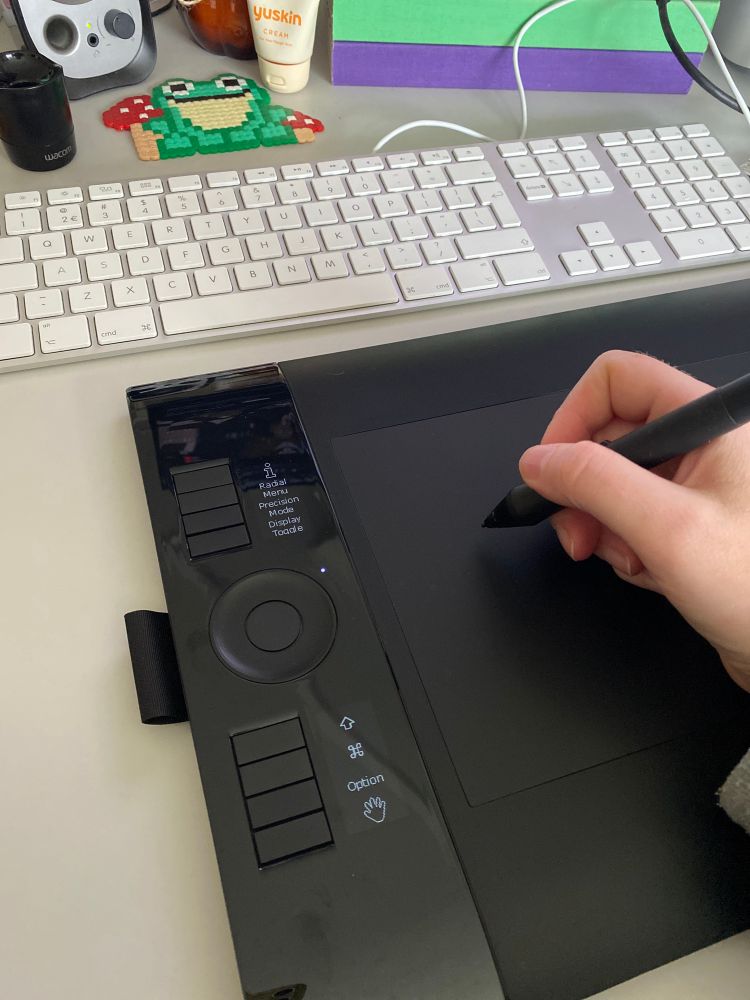 Photo of a zoomed in desk with an intuos 4 tablet and a hand with a pen next to an apple keyboard