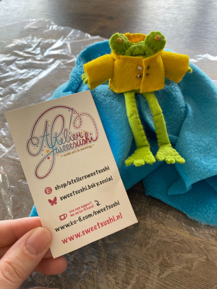 Floris the frog in his yellow rain coat with a business card from Atelier Sweet Sushi next to it