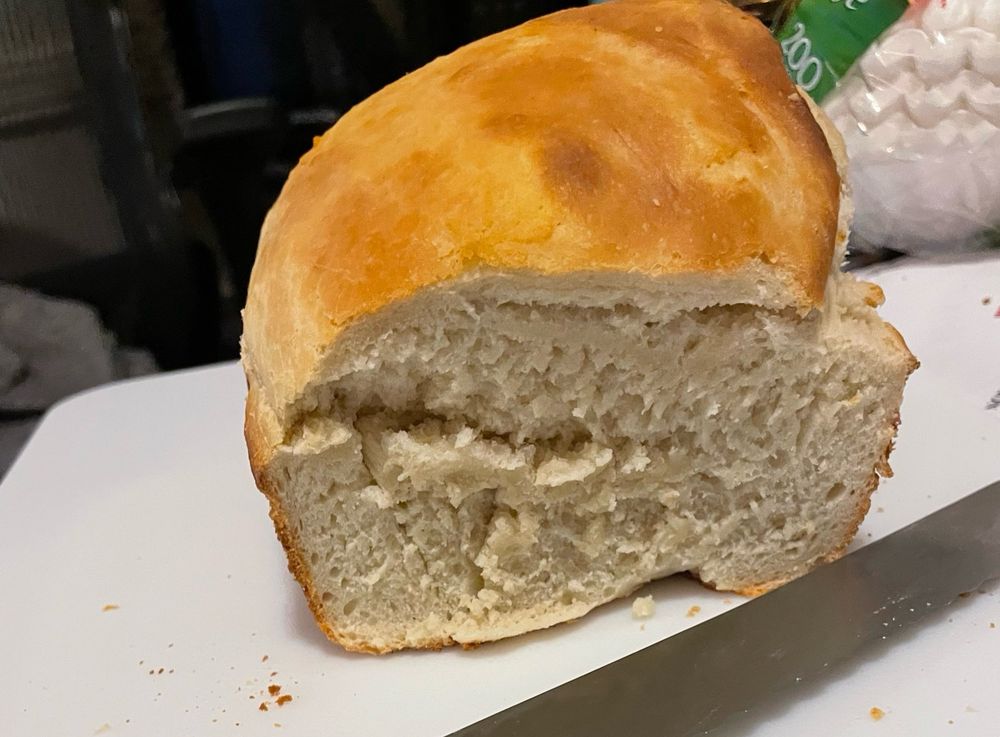 Loaf of bread with one piece missing so you can see the inside. It’s on a cutting board and there’s a bread knife in the foreground and coffee filters in the background because my kitchen is a mess
