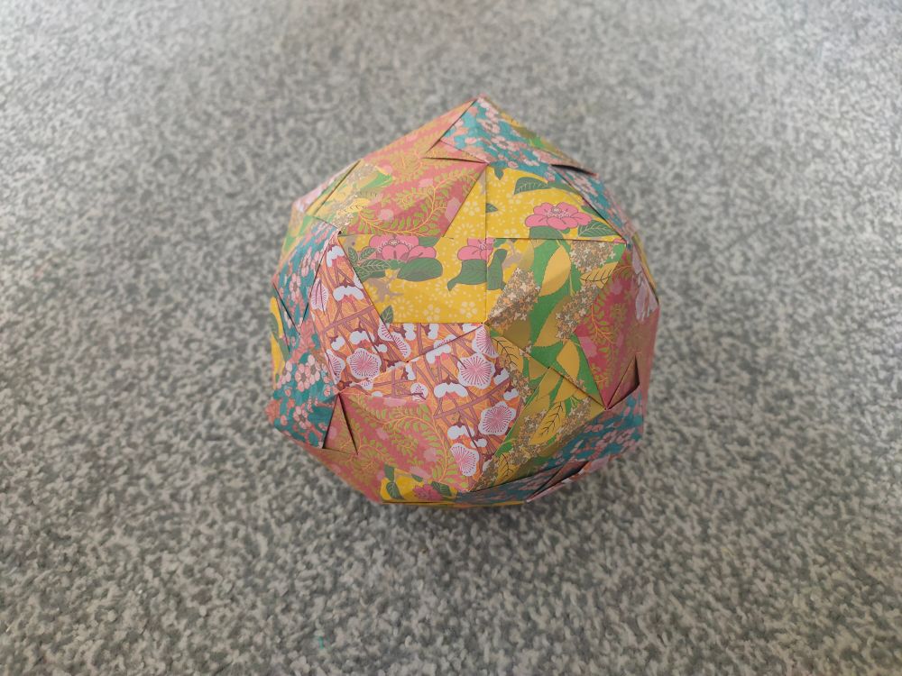 Outside of triacontahedron made with colourful, patterned origami paper on a grey carpet.