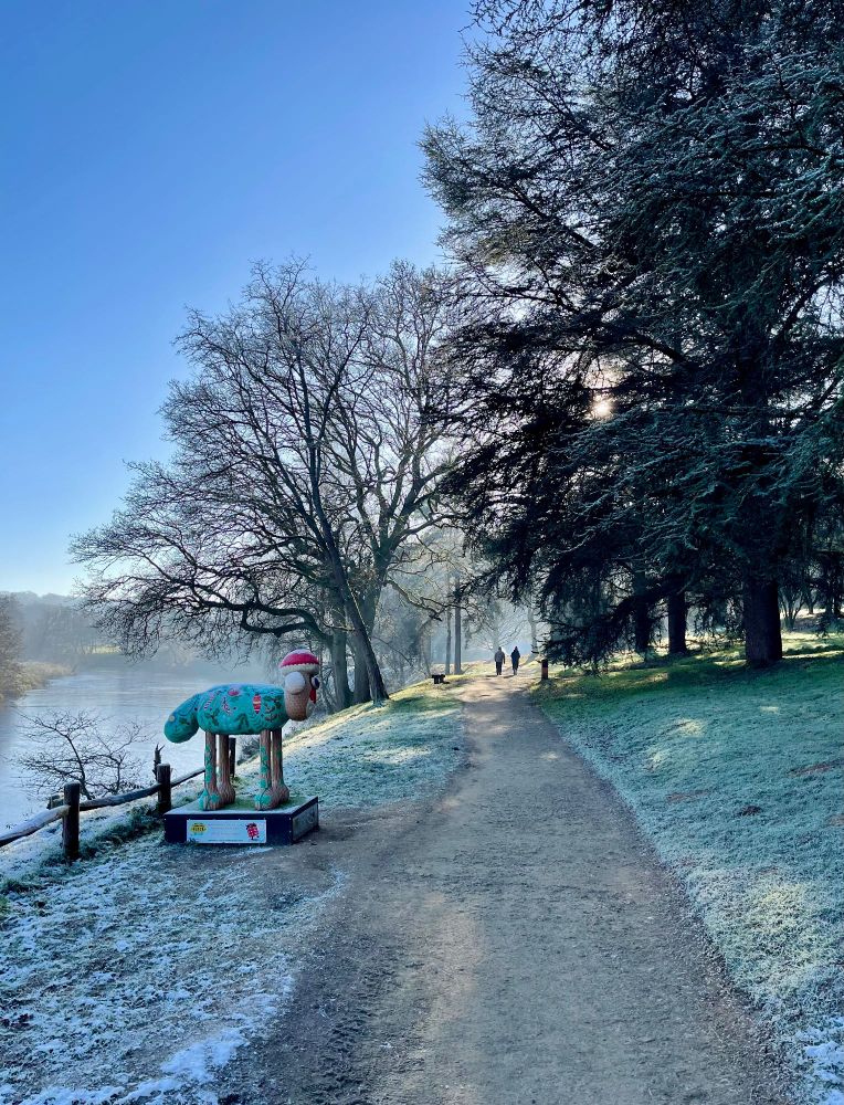Photo of two people walking by a lake on a frosty morning with a Shaun the sheep statue in the foreground 