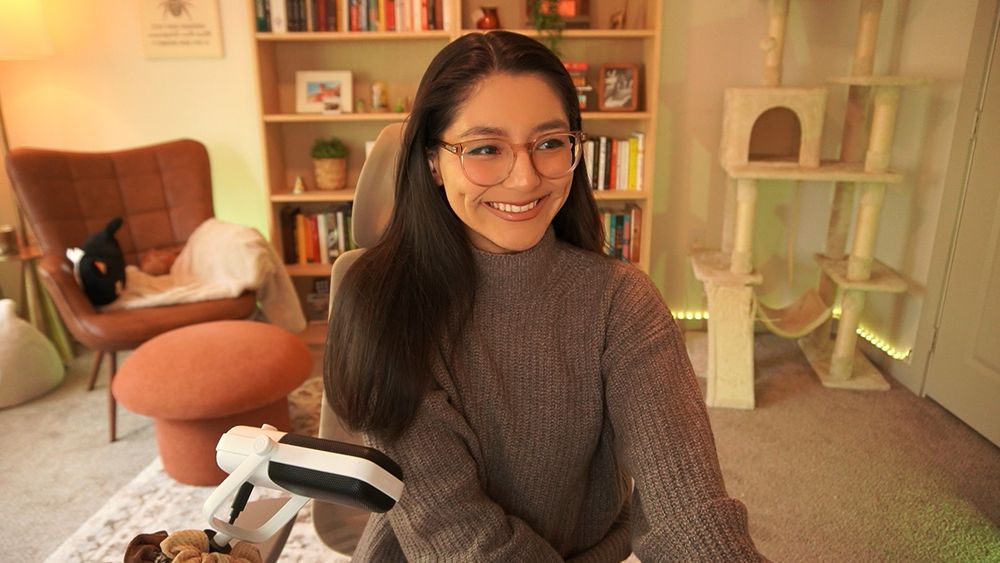 Jules has a wide smile and is wearing a toffee sweater. The office is lit in a yellow-green hue