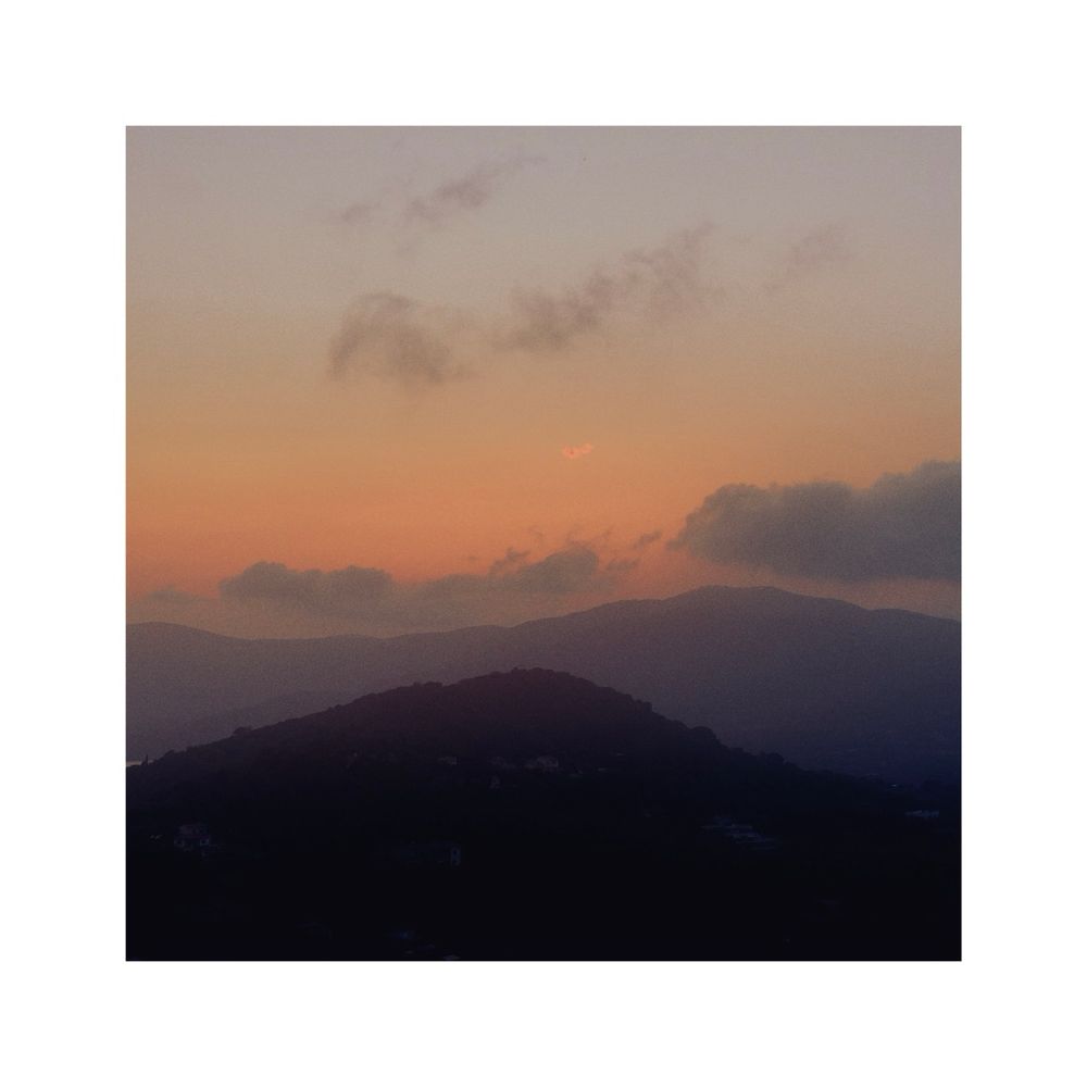 sunset over the hilly coastline of elba, tuscany, italy. the sky as well as the more distant hills are tinted in different shades of red. the sky is partly covered with clouds that seem to have similar tones as the hills