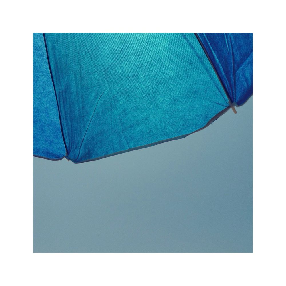 looking at parts of a blue sun umbrella against the turquoise sky. you can still see the sun peeking through the fabric of the round parasol