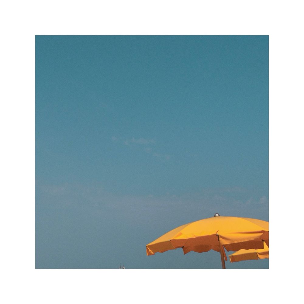 a tiny yellow sun umbrella is sitting in the bottom right corner of the square image. all the rest of the frame is just focusing on the crystal clear turquoise sky