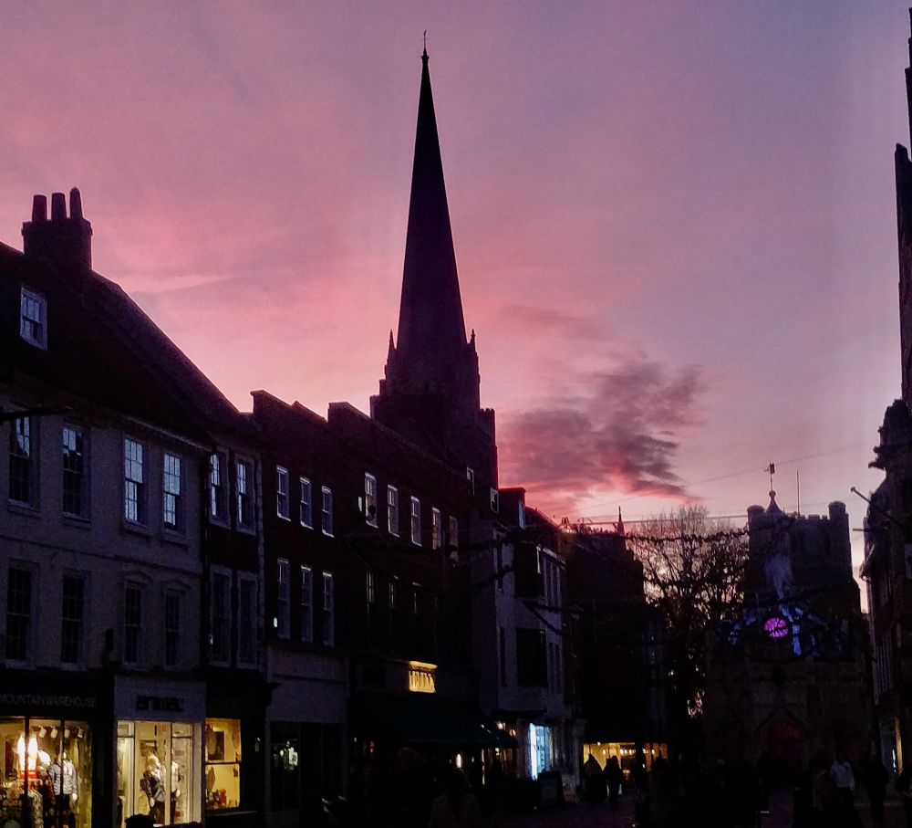 A view taken just after sunset in East Street (Chichester) looking west, with a deep red sky. The row of buildings on the left of there photo mostly date from the 18th century. The Market Cross, its clock dial illuminated with a purple glow, was built in 1501. It stands and the meeting-point of the four main streets of medieval Chichester - East, South, West and North Streets, which radiate in from the former positions of the Roman and medieval city gates.