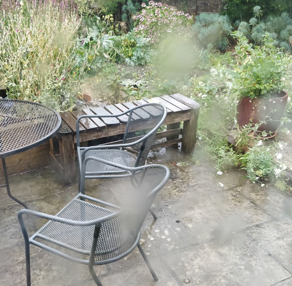 A back garden and furniture in heavy rain, photographed through glass.  The fuzzy patches on the image are caused by rain on the glass.
