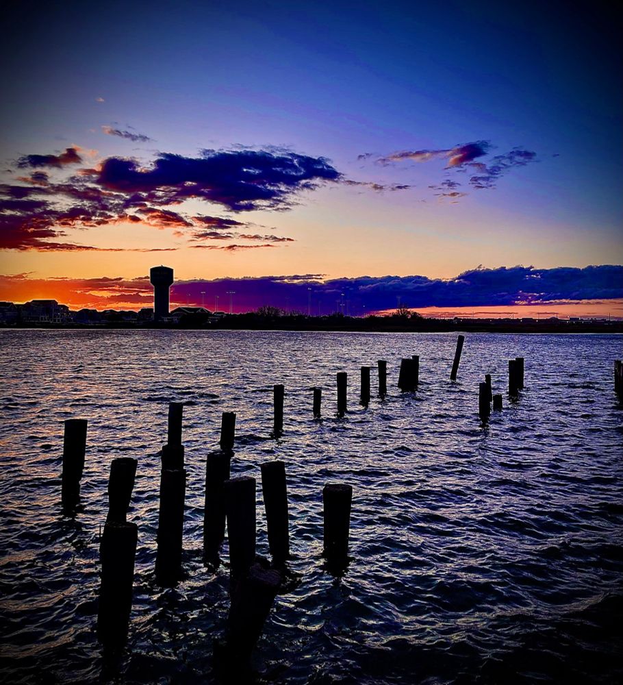 Sunset over the bay. Old pilings stick out of the water. 