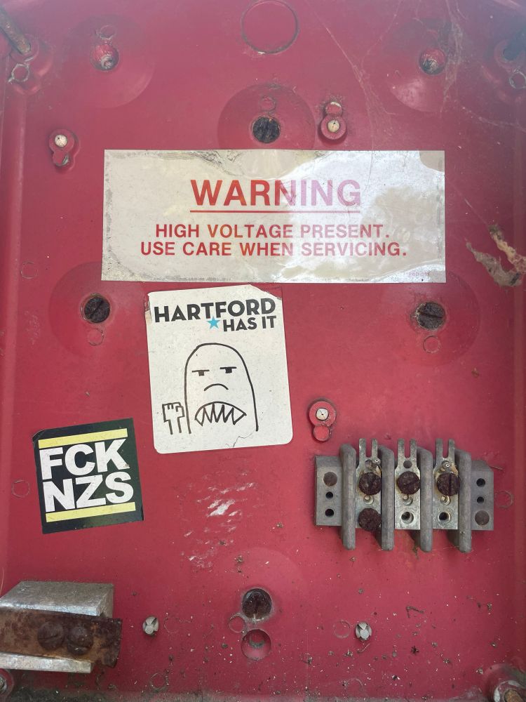 Interior of street corner electrical box with high voltage warning and stickers that say Hartford Has It and FCK NZS.