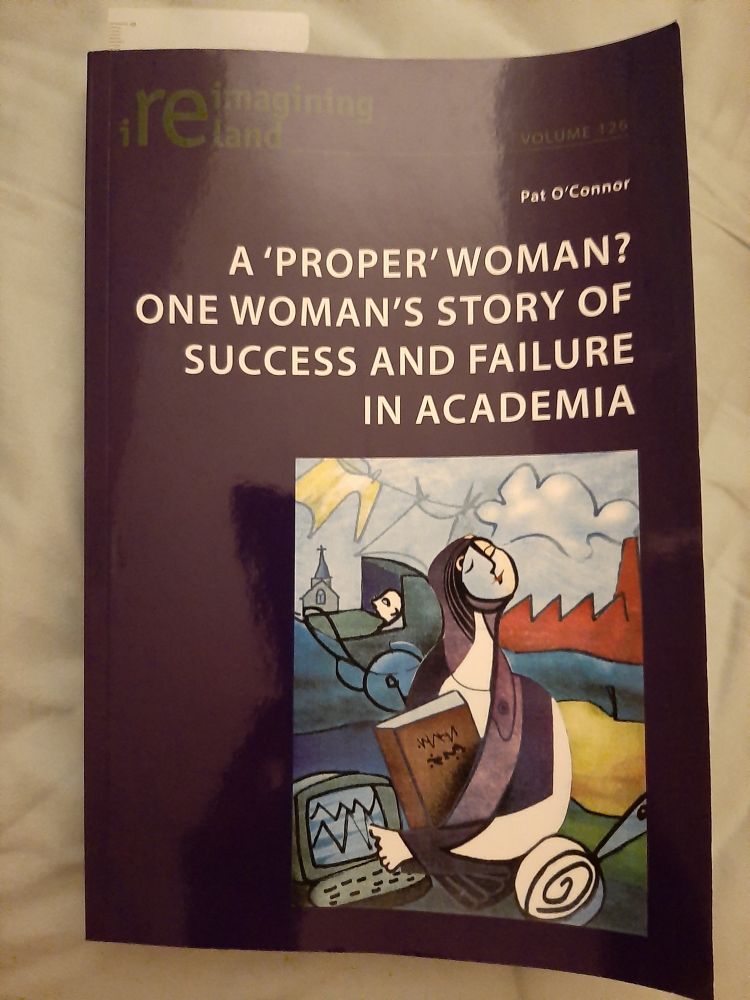 Book "A ‘proper’ woman? One woman’s story of success and failure in academia" by Pat O'Connor, lying front cover up on a blue background. Cover of the book is navy with white writing. Colourful image in the bottom right hand corner contains images of a woman holding a book, pointing to a computer with a church & baby in a pram in the background.

