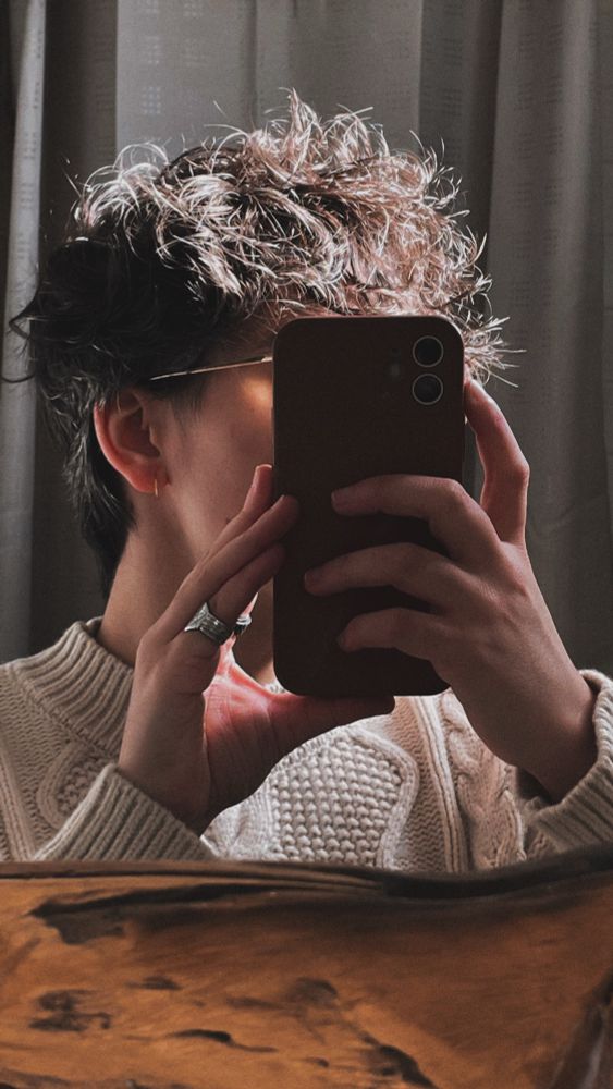 a mirror selfie, I am holding my phone which is hiding my face but shows my fluffy hair and my creme warm sweater